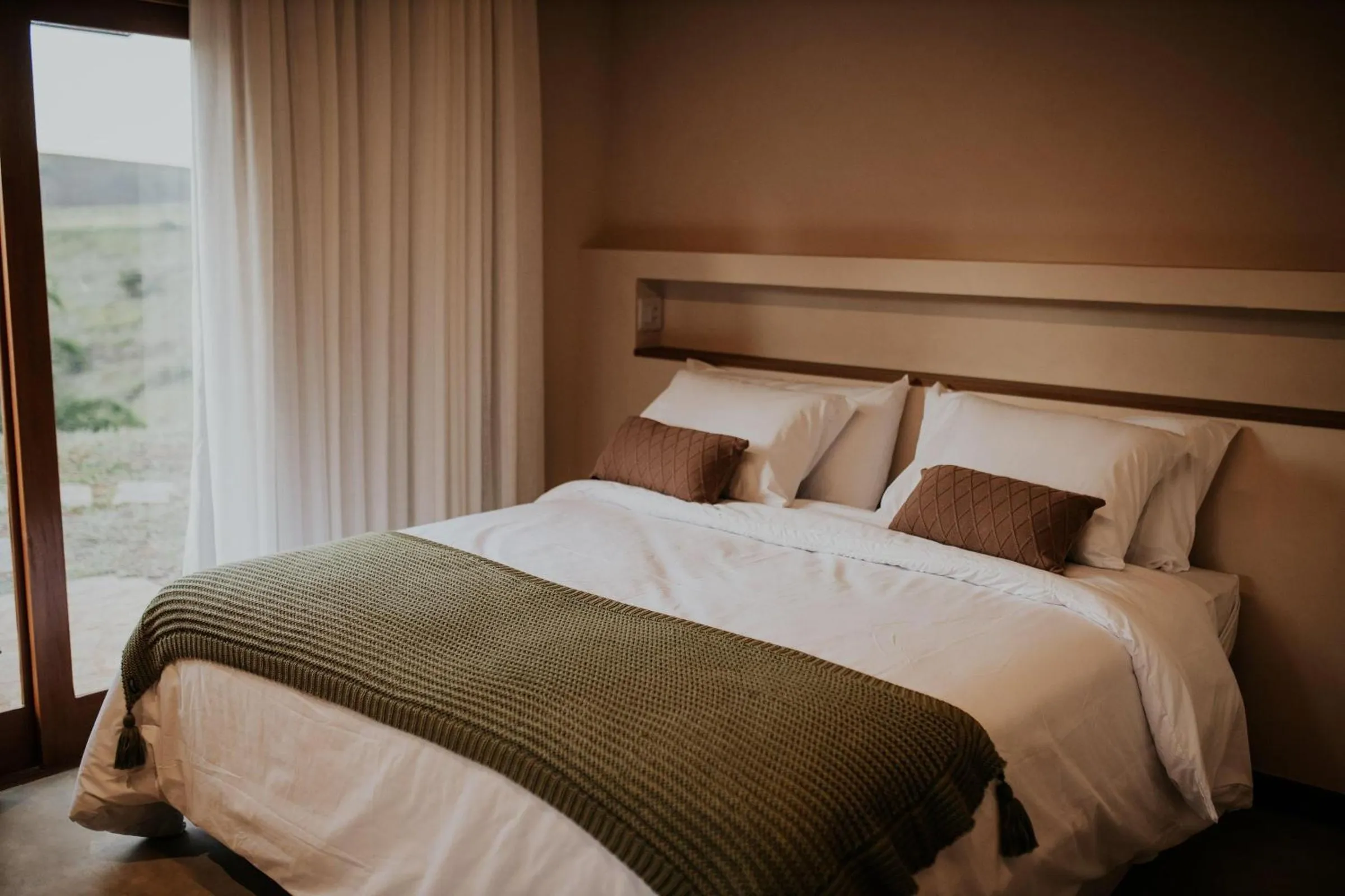 Suíte da cabana com cama de casal e janela para o vinhedo